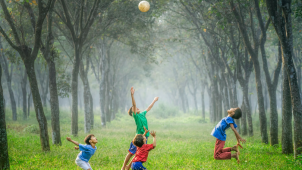 children playing outdoors jumping and reaching for a ball